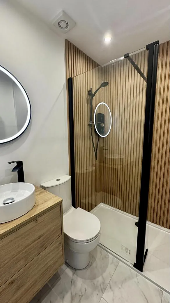 A bathroom with a slatted oak shower wall, black framed screen and round LED mirrors