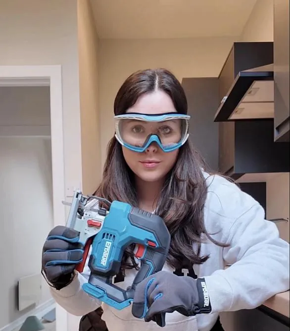 Emma in safety goggles holding a cordless jigsaw on site